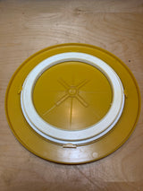 Bee Plastics harvest gold lazy Susan tray featuring a round design with an “X”-shaped rib pattern and a removable white gasket insert for secure sealing.