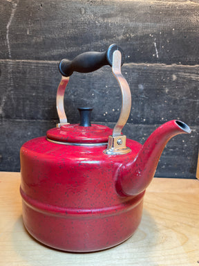 Tea kettle - steel red speckled enamelware - Paula Deen, featuring a curved spout and black-grip metal handle, on a wood surface. Durable, vibrant addition to kitchens.