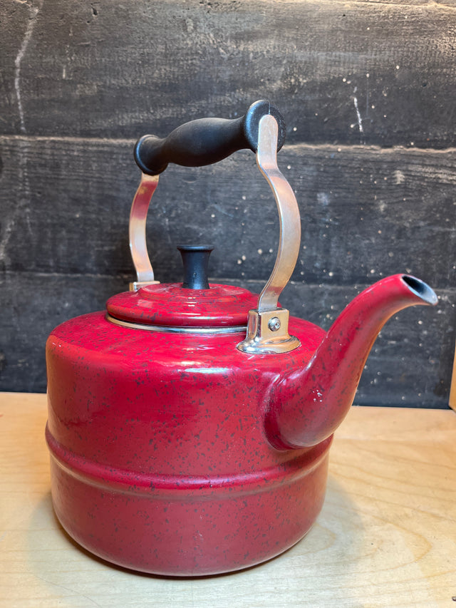 Tea kettle - steel red speckled enamelware - Paula Deen, featuring a curved spout and black-grip metal handle, on a wood surface. Durable, vibrant addition to kitchens.