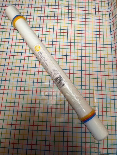 Fondant roller with guide rings - Wilton new in packaging, featuring a white plastic design with silicone guides, on a grid-patterned surface.