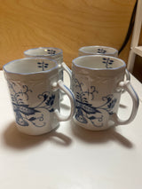 1986 Arnhart set of 4 Blue Onion coffee mugs with ornate handles, embossed floral rims, and slightly angular sides on glossy white ceramic featuring blue illustrations.