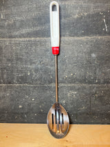 Pedrini stainless steel slotted serving spoon with a long handle, featuring a white plastic grip, red collar, and slender metal shaft for effective draining.