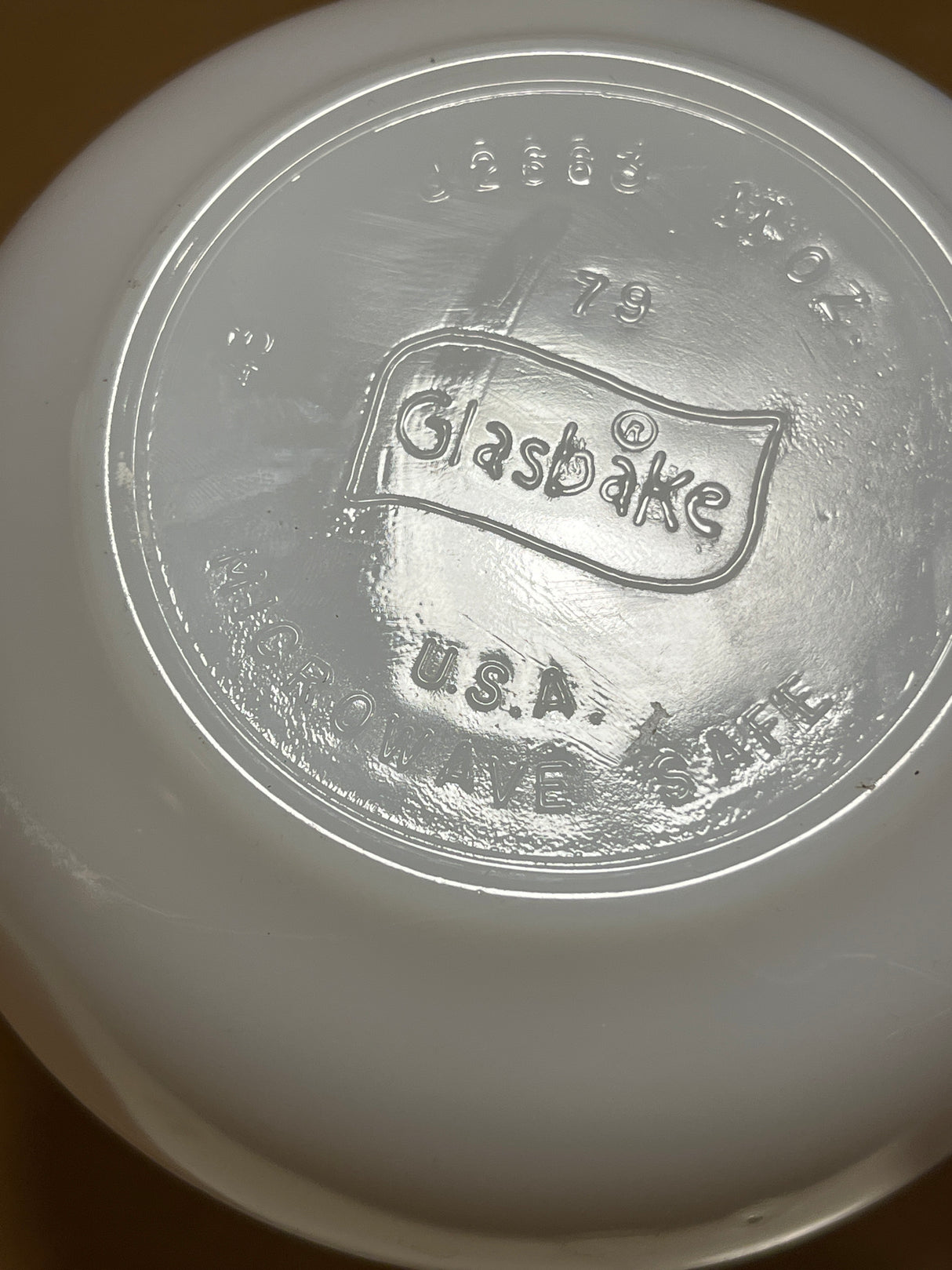 Underside of a Glasbake milk glass soup or casserole bowl with handle, featuring Glasbake USA Microwave Safe and model number in raised lettering.