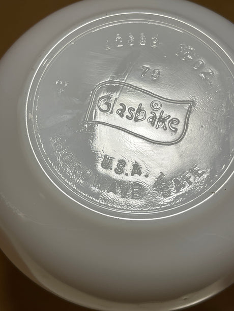Underside of a Glasbake milk glass soup or casserole bowl with handle, featuring Glasbake USA Microwave Safe and model number in raised lettering.