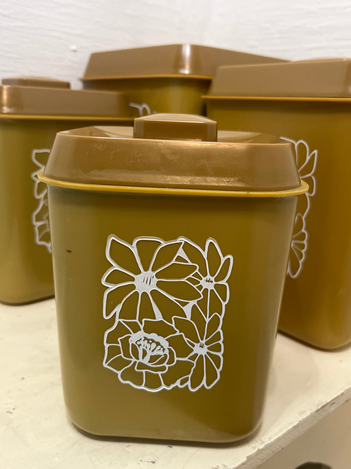 Melmac set of 4 retro food storage containers with mustard color and white floral illustrations, highlighting a cracked second-largest container, arranged on a shelf.