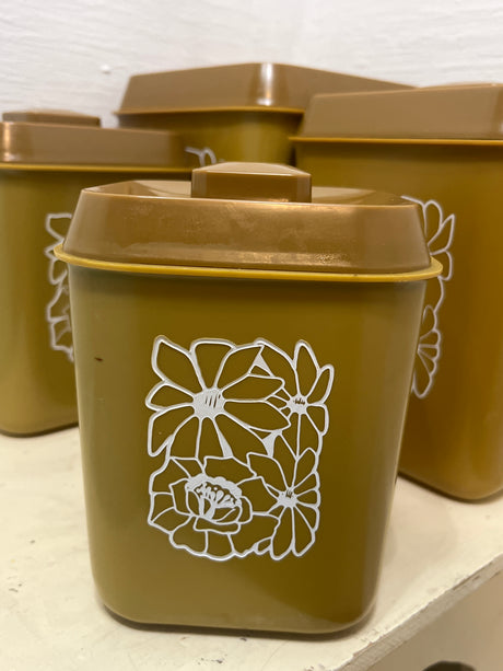 Melmac set of 4 retro food storage containers with mustard color and white floral illustrations, highlighting a cracked second-largest container, arranged on a shelf.