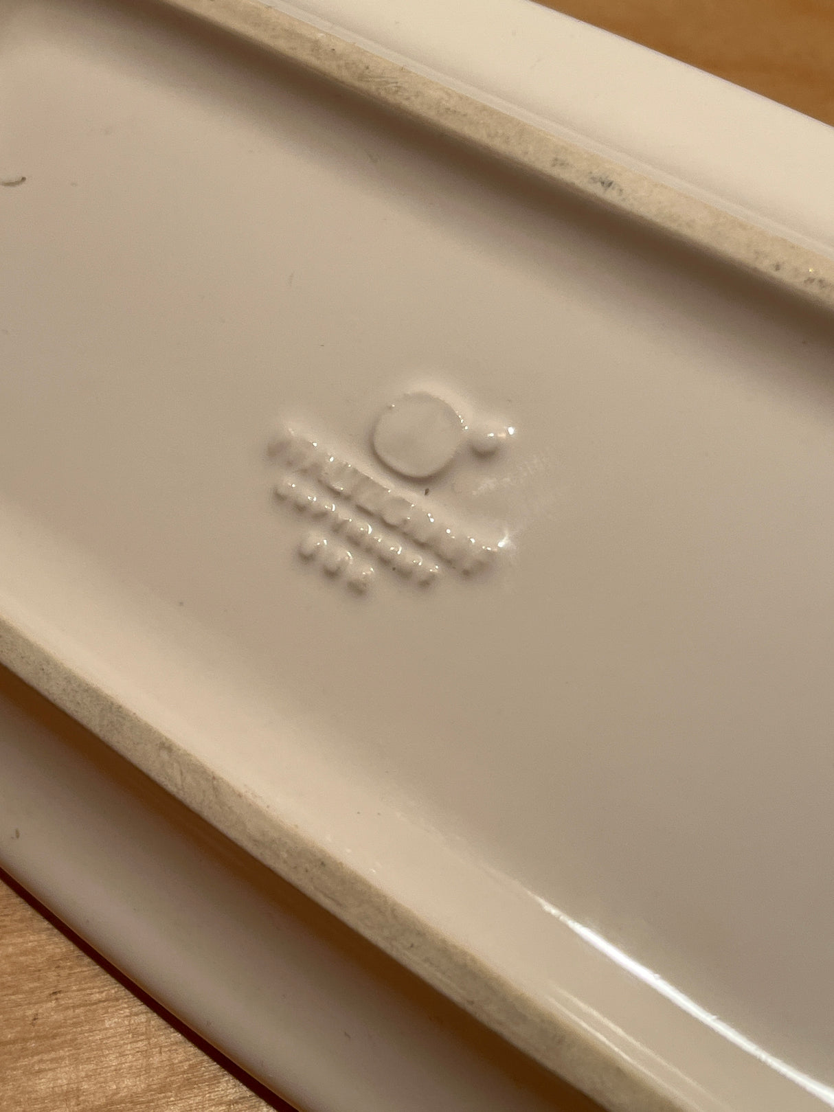Underside of a Pfaltzgraff covered white ceramic butter dish, showing central boss and factory stamp with logo and model markings on glazed surface.