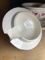 Porcelain soup tureen bowl with lid, underplate, and ladle, hand-painted with red roses, displayed on a wood shelf; note minor chips on the rim.