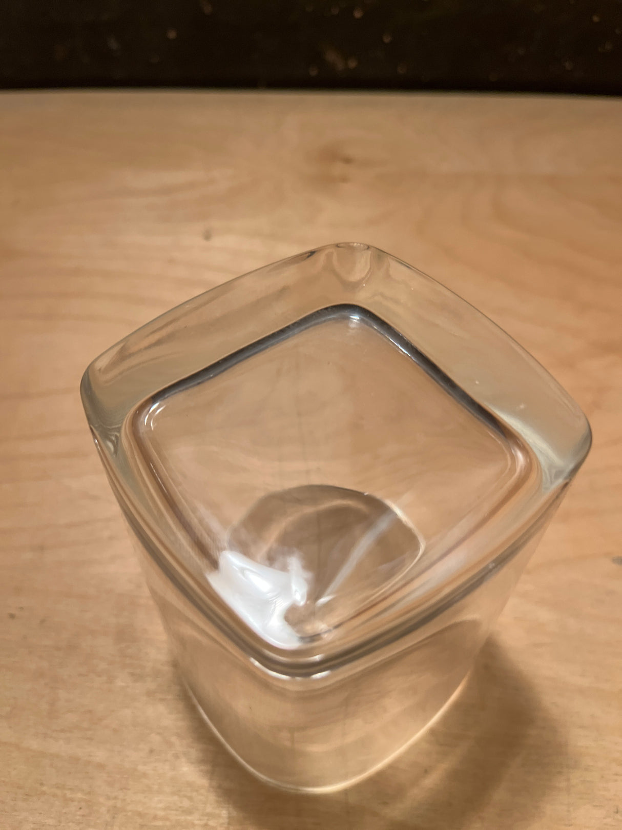 Square heavy bottom tumbler drinking glass shown upside down on a light wooden surface, highlighting its clear, robust design and compact form.