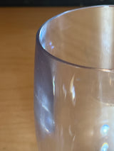 Stemless hard acrylic wine glass on a wooden surface, showcasing its clear design with light reflections on the rim and side wall.