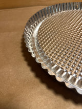 Pampered Chef stainless steel flan pan, featuring a round, fluted design ideal for pies or tarts, ensures even baking and easy unmolding with its textured surface.