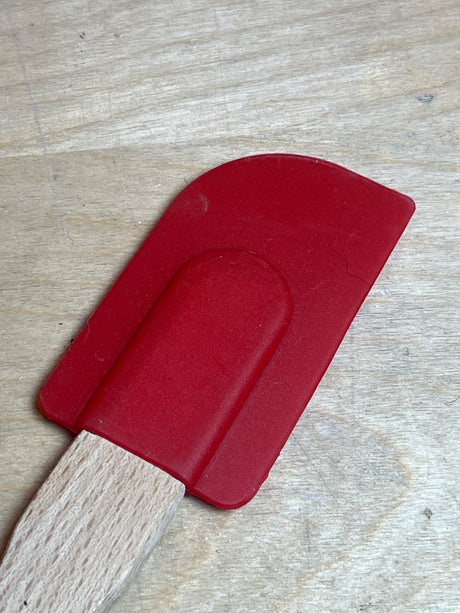 Silicone spatula - red Farberware with wood handle, featuring a flexible silicone blade on a short wooden handle, displayed on a wooden surface.