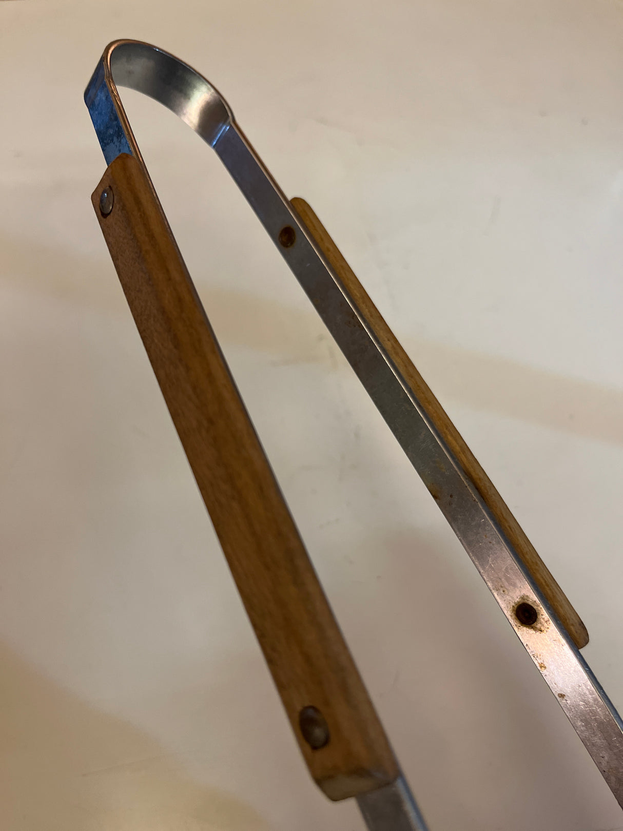 Vintage grill tongs with wood handle featuring metal arms and a spring-style loop for easy operation, ideal for kitchen and serving tasks.
