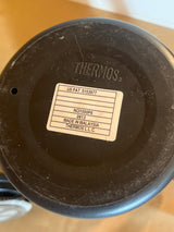Underside view of a Thermos Nissan stainless steel insulated French press coffee maker, featuring the embossed logo, patent number, and manufacturing details on a white label.