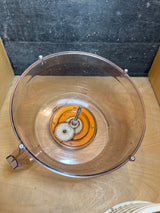 Spinner food processor work bowl, disassembled, showing an empty clear plastic bowl with a central drive shaft and visible white plastic gears for blade connection.