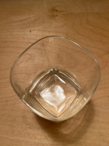 Square heavy bottom tumbler drinking glass on a wooden surface, showcasing its clear, square design and robust base, with light reflections hinting at subtle elegance.