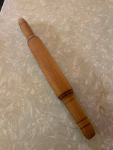Wooden belan rolling pin with a grooved surface rests on a countertop, designed for efficient dough rolling.
