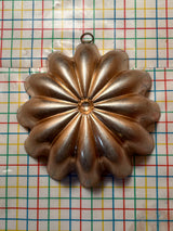 Copper-lined aluminum mold for jello, shaped like a multi-petaled flower, with a small hanging ring at the top for easy display.