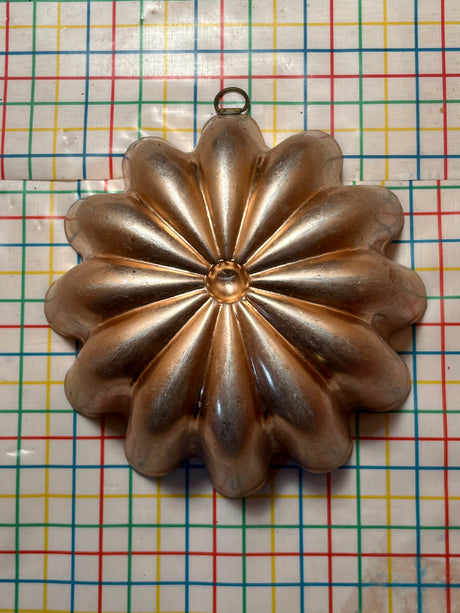 Copper-lined aluminum mold for jello, shaped like a multi-petaled flower, with a small hanging ring at the top for easy display.