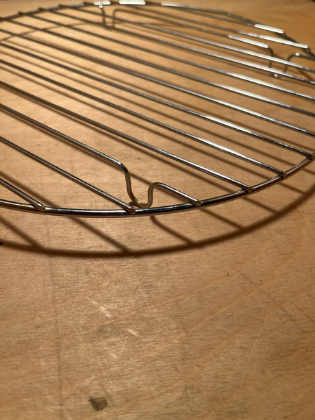 Circular wire rack for cooling, roasting, or campfire cooking on a wooden surface, suitable for ovens, air fryers, and toaster ovens.
