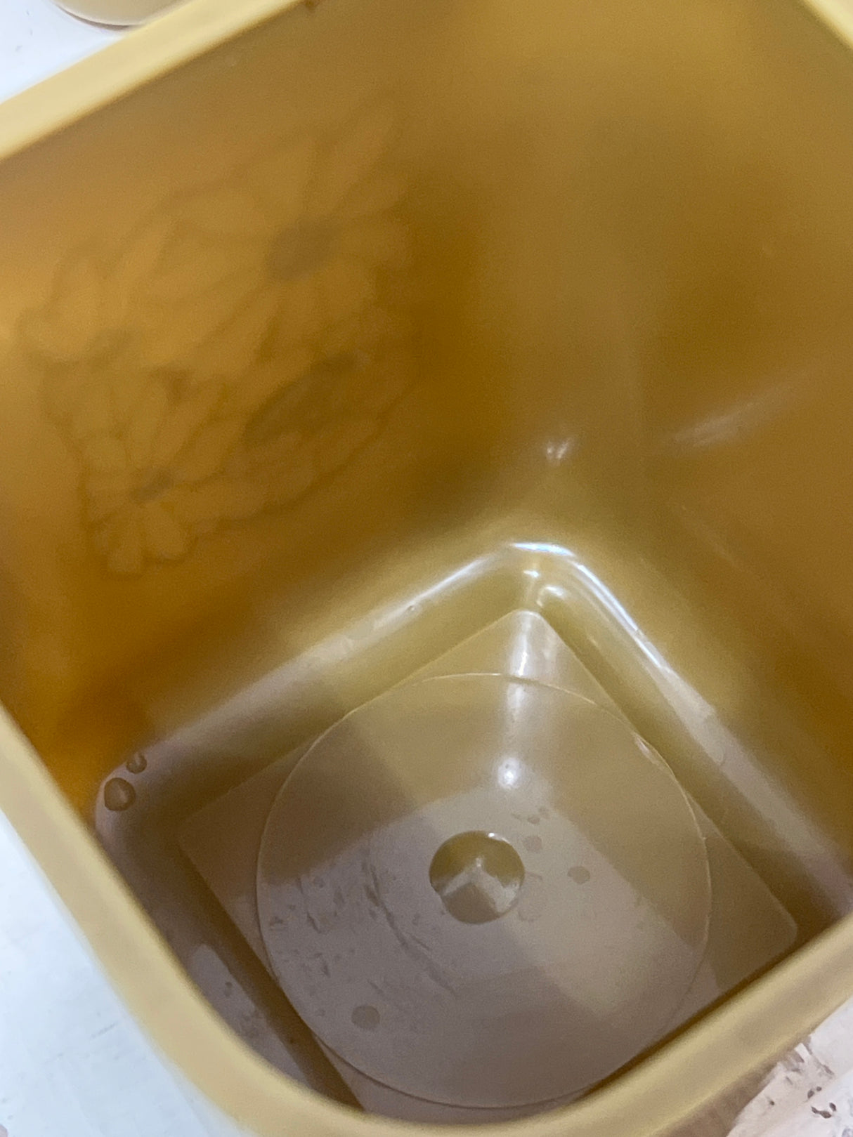 Interior of a Melmac set of 4 retro food storage containers, showing a mustard-yellow bin with clear insert and embossed floral motif, slight liquid visible.