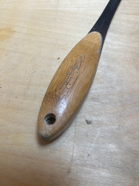 Wolfgang Puck stainless steel perforated spatula with bamboo handle, showcasing a thin metal blade, rounded wooden handle with hanging hole, and engraved logo.