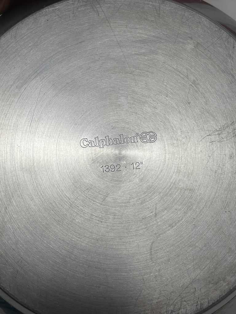 Close-up of Calphalon heavy-duty 12-inch stainless steel frying pan with insulated handle, showcasing its circular metal surface with engraved numbers.