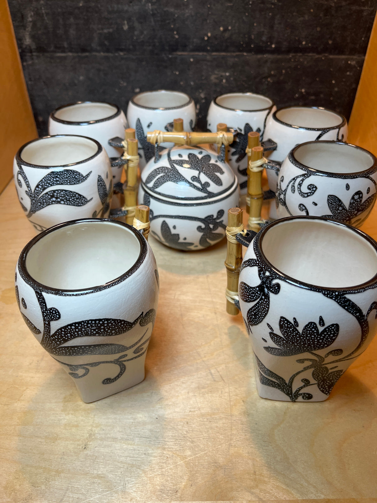 Set of 8 white mugs and sugar bowl with lid featuring floral pattern, arranged on bamboo rack, showcasing ceramic craftsmanship and decorative stippled design.