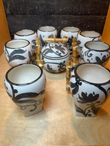 Set of 8 white mugs and sugar bowl with lid featuring floral pattern, arranged on bamboo rack, showcasing ceramic craftsmanship and decorative stippled design.