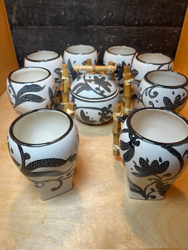 Set of 8 white mugs and sugar bowl with lid featuring floral pattern, arranged on bamboo rack, showcasing ceramic craftsmanship and decorative stippled design.