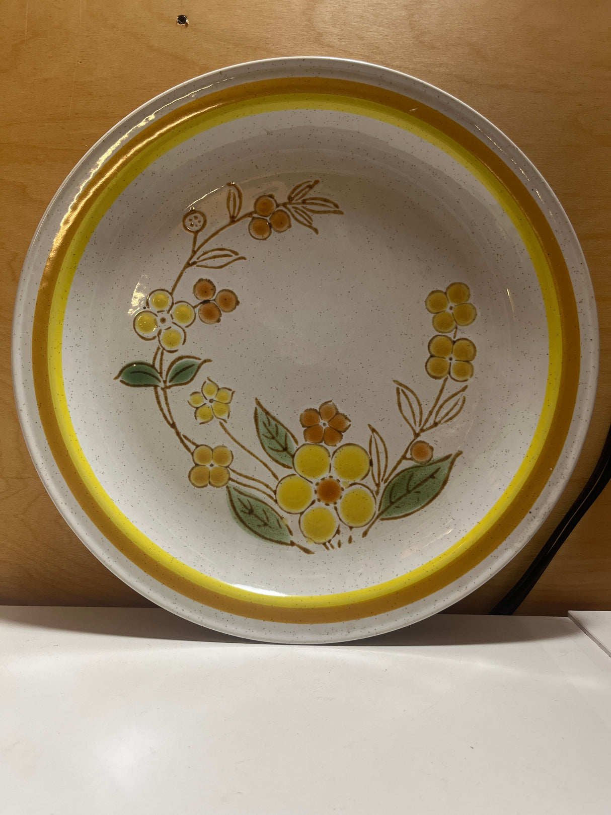 Sunny speckled floral serving plate featuring a ceramic design with a yellow floral motif, gold and orange rim, and painted leaves from International China’s Country Meadow line.