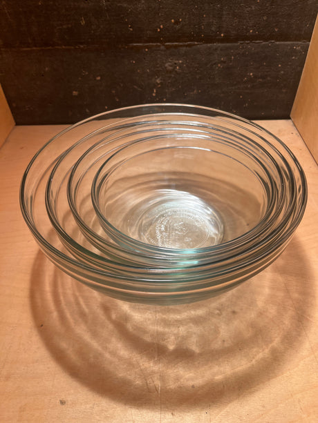 Set of 4 glass mixing bowls - Anchor Hocking, stacked by size on a wooden surface, showcasing their clear glass design for versatile kitchen use.