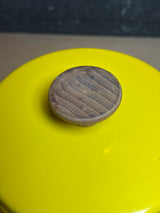 Close-up of a Fondue pot - vintage Michael Lax Copco - yellow enamel, featuring a round wooden knob with carved grooves on the lid.