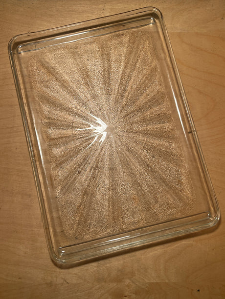 Rectangular glass serving tray with sunburst pattern, featuring fine sand trapped between glass sheets, creating dynamic dune-like designs as it tilts.