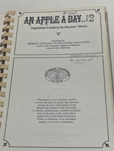 Title page of 'RARE An Apple A Day Volume Two – Vegetarian Cookery by Doctors' Wives' with publisher and emblem, featuring handwritten notes.