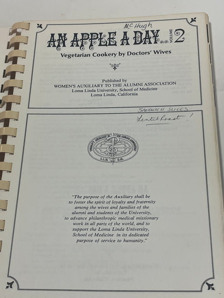 Title page of 'RARE An Apple A Day Volume Two – Vegetarian Cookery by Doctors' Wives' with publisher and emblem, featuring handwritten notes.
