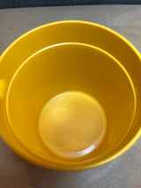 Tupperware golden yellow pitcher, empty and viewed from above, resembles a small bucket-style container on a light wood surface.