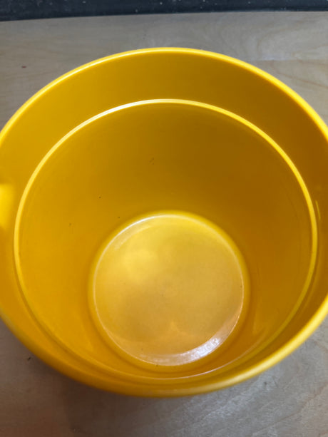 Tupperware golden yellow pitcher, empty and viewed from above, resembles a small bucket-style container on a light wood surface.