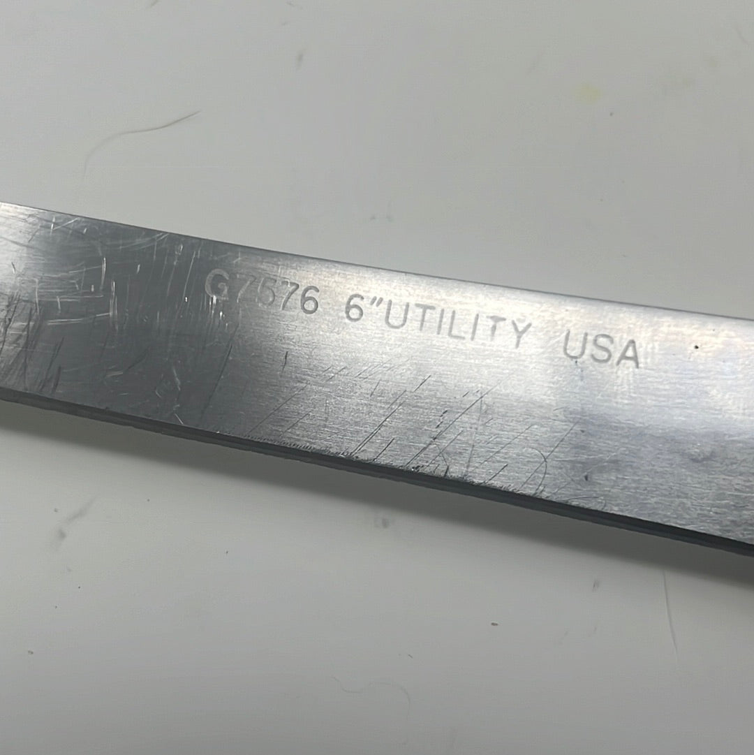 A close-up of the EKCO Forge Utility 6 Inch Knife, showcasing its narrow, long blade with text and metal surface details, ideal for slicing meat, fruit, and veggies.