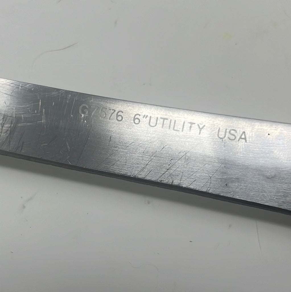 A close-up of the EKCO Forge Utility 6 Inch Knife, showcasing its narrow, long blade with text and metal surface details, ideal for slicing meat, fruit, and veggies.