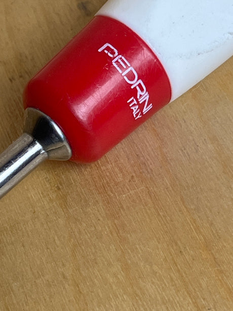 Close-up of Pedrini stainless steel slotted serving spoon handle, showcasing the red and white grip with PEDRINI ITALY stamped, attached to a metal shaft.