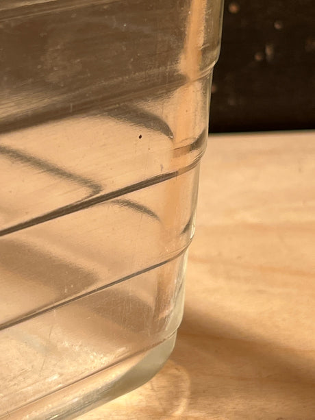 Close-up of a Glass ribbed loaf baking pan, vintage Glasbake style #59, showing its horizontal ridges and a small water pool on a wooden surface.