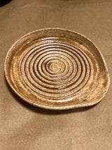 Handmade ceramic garlic grater spoon rest by Charles Lehman, featuring a speckled brown glaze and concentric ridges, displayed on a neutral tabletop.