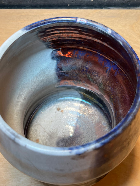 Handmade ceramic utensil holder/vase with an iridescent glaze, showcasing smooth, rounded form on a wooden surface, ideal for small utensils or decorative use.