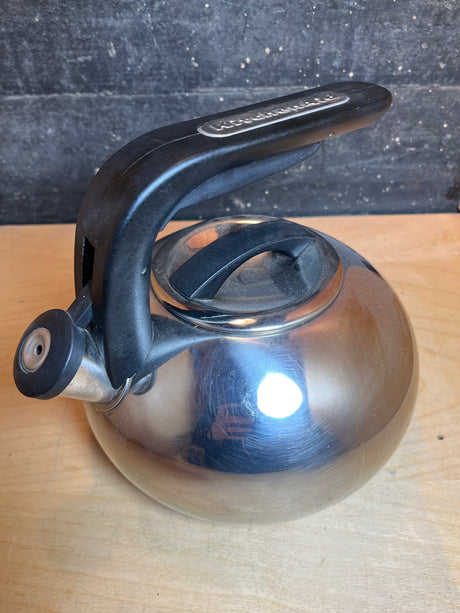 Whistling tea kettle - Kitchenaid 2 quart / 1.9L stainless steel with black handle, featuring a domed lid and arched handle, sits on a wooden surface.