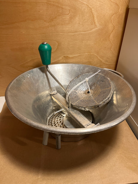 Louis Teller 3.5qt rotary food mill potato ricer featuring a metal bowl, green-handled crank, and interchangeable perforated discs, secured with a plastic cable tie.