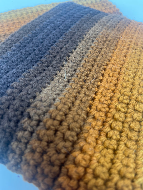 Close-up of a hand-crocheted potholder with a chunky texture, ideal for gripping hot cookware. The set includes two retro brown striped potholders.