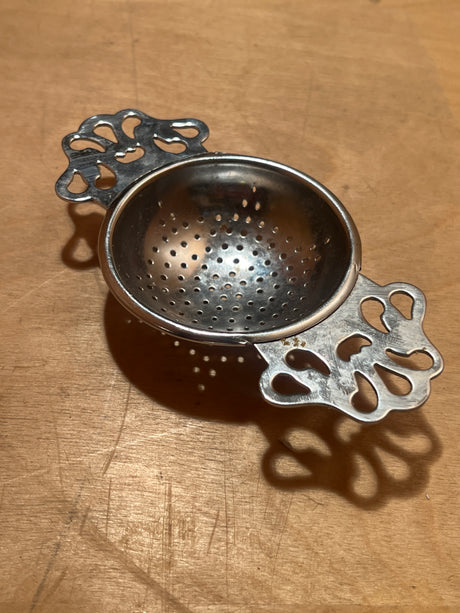 Tea strainer - vintage midcentury modern Japanese silver plated, features decorative handles and a perforated bowl for efficient loose-leaf tea steeping on a wooden surface.