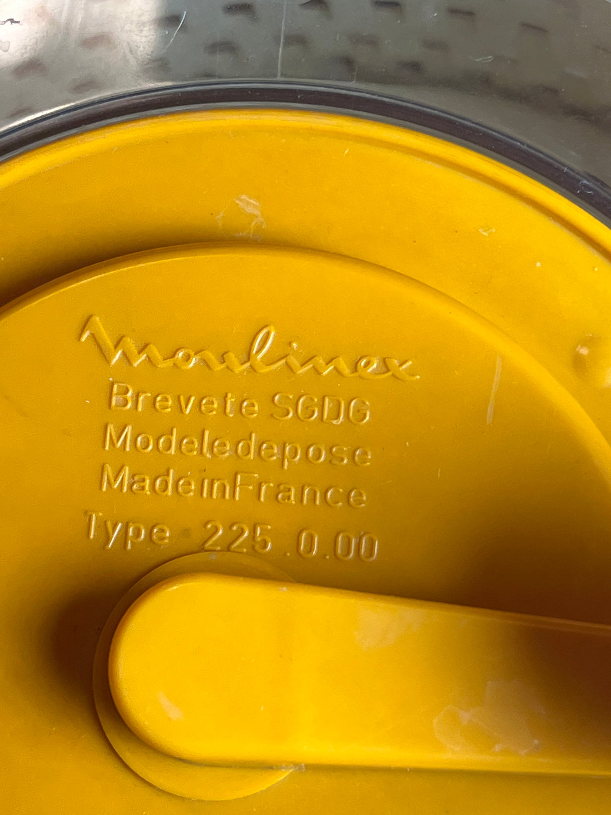 Close-up of a yellow lid from a Moulinex Spinner kitchen appliance, featuring embossed details including brand name, model number, and Made in France.