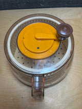 Spinner: A manual salad spinner with a hand crank, featuring a clear plastic bowl and an inner perforated basket for drying greens efficiently.